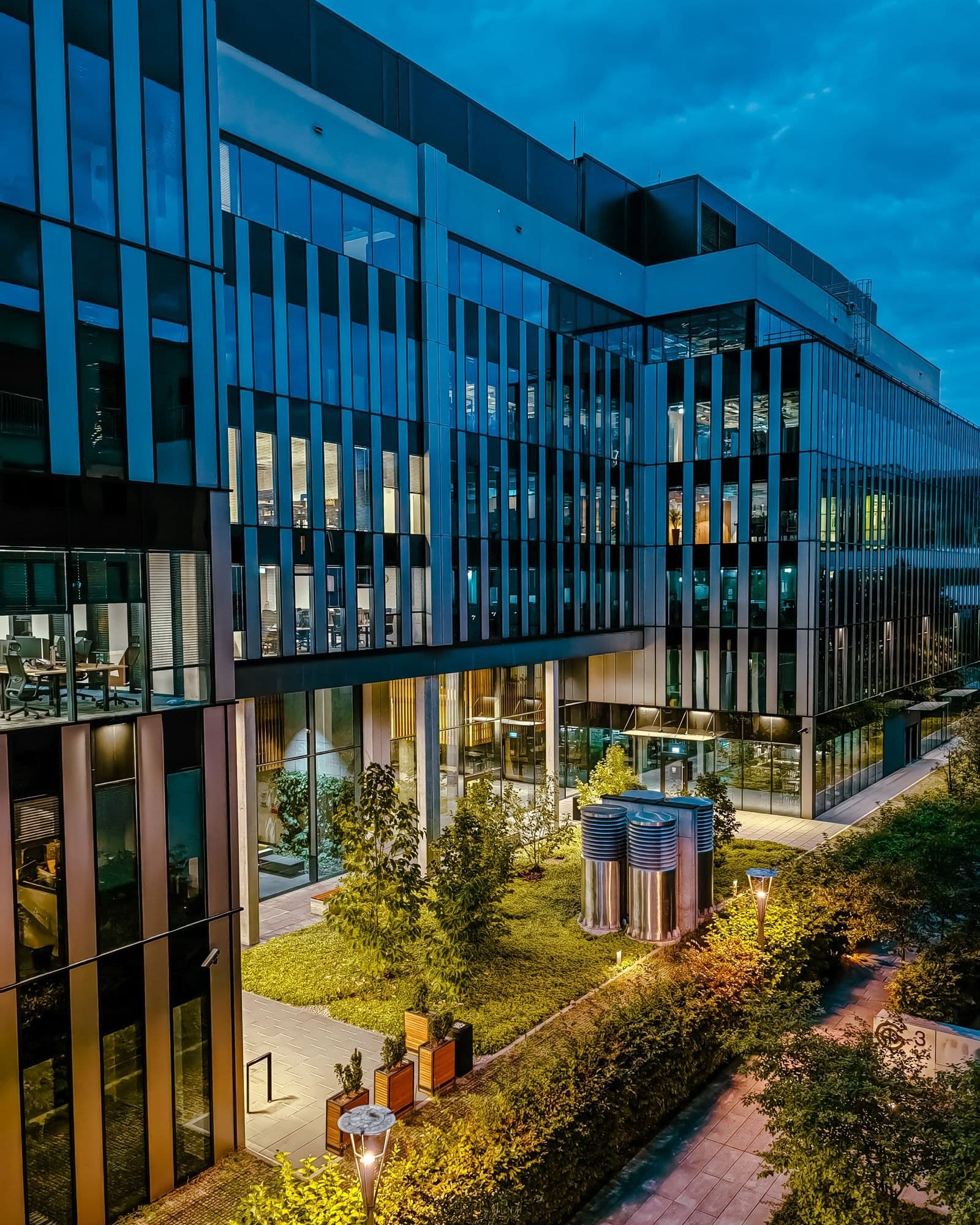 Modern glass office building at dusk, with lit interiors looking onto a courtyard